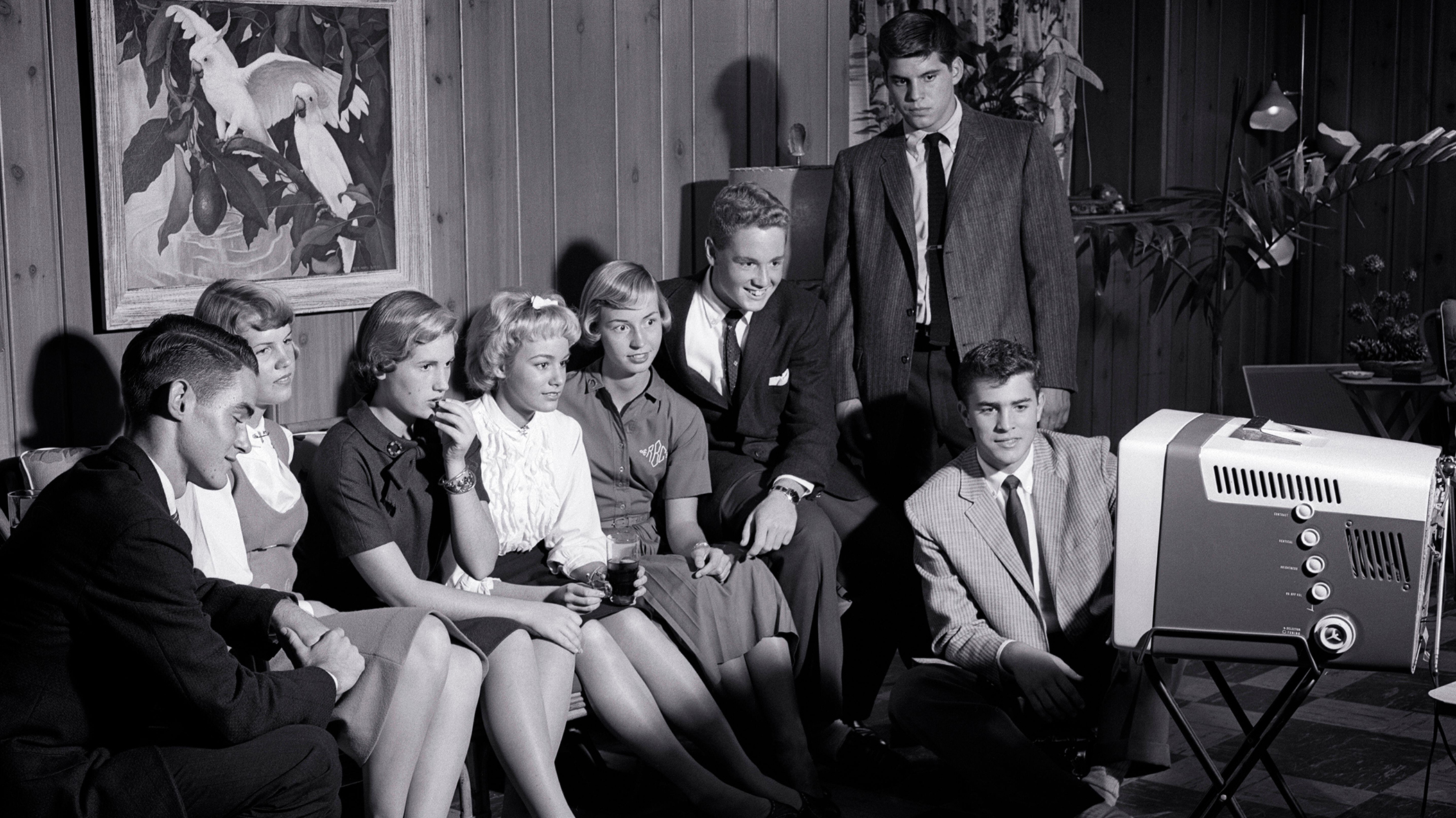 A black-and-white photograph from the 1950s showing teens watching TV in a living room