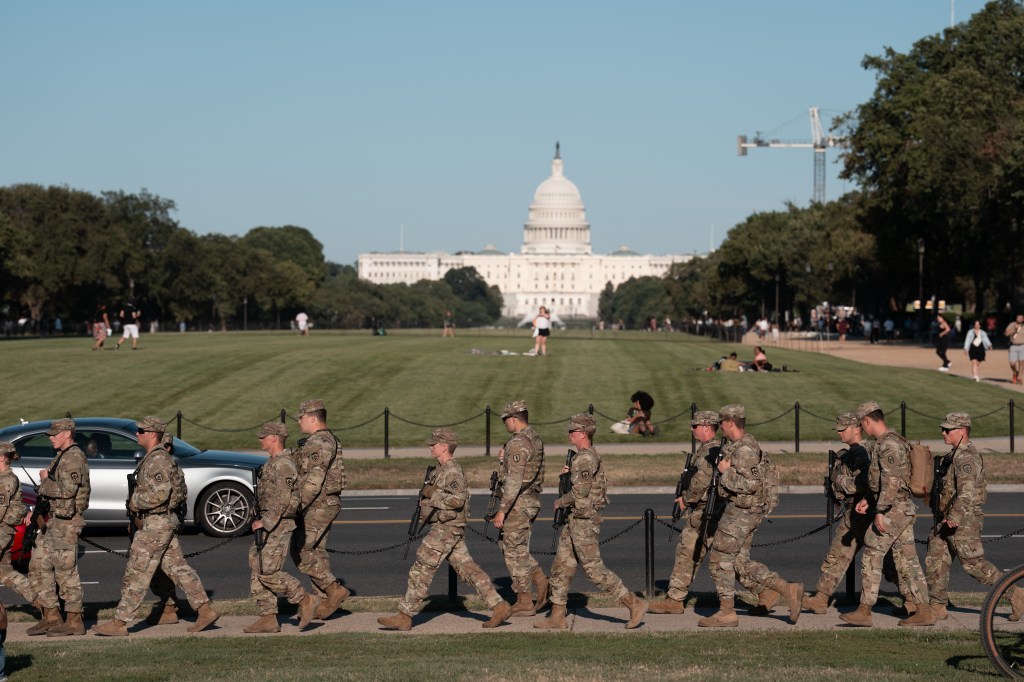National Guard troops patrolling the National Mall in Washington, D.C., with the Capitol building in the background.