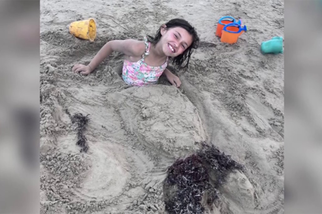 Girl buried in sand on beach.