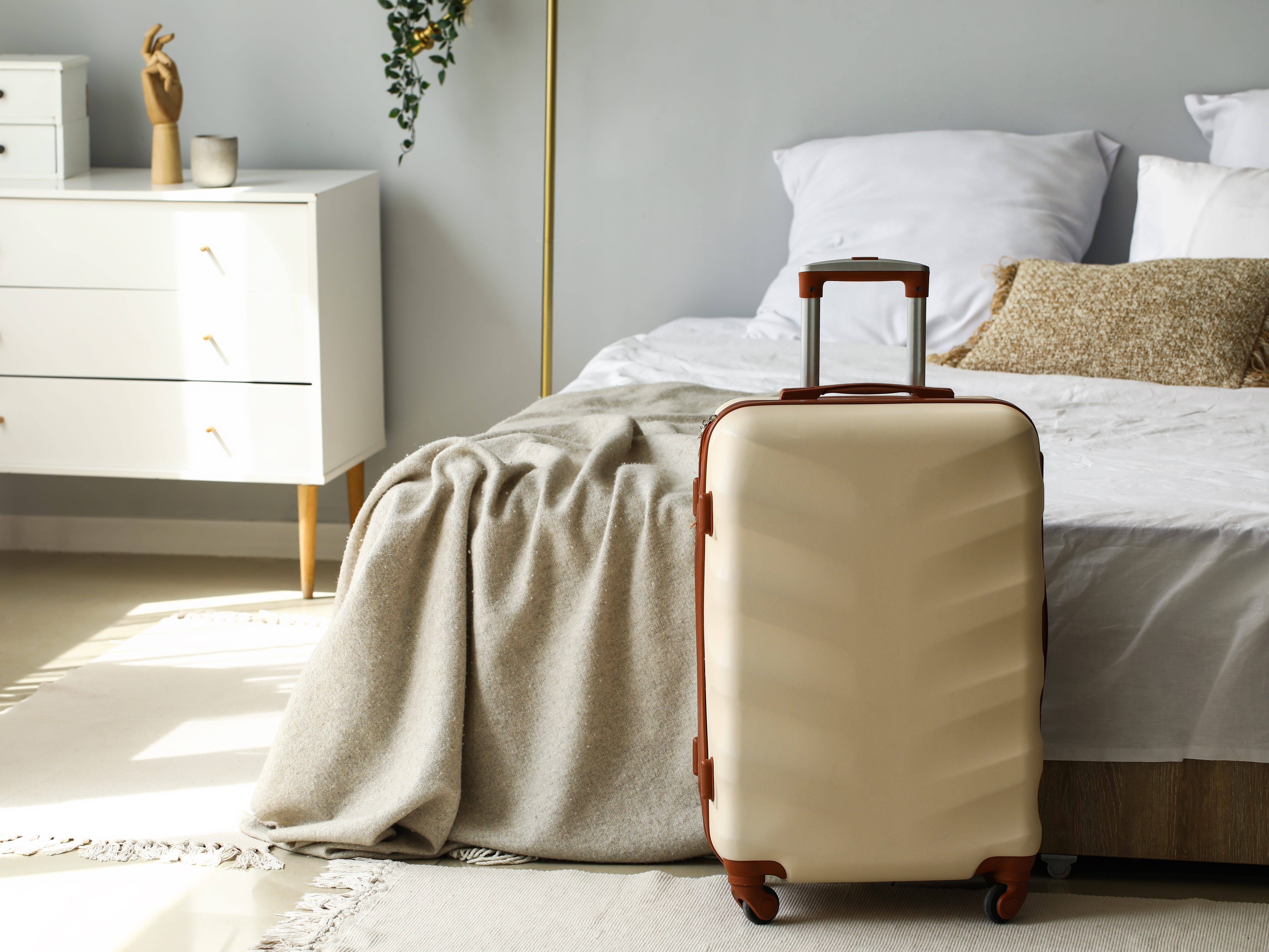 A beige suitcase placed upright at the foot of a bed.