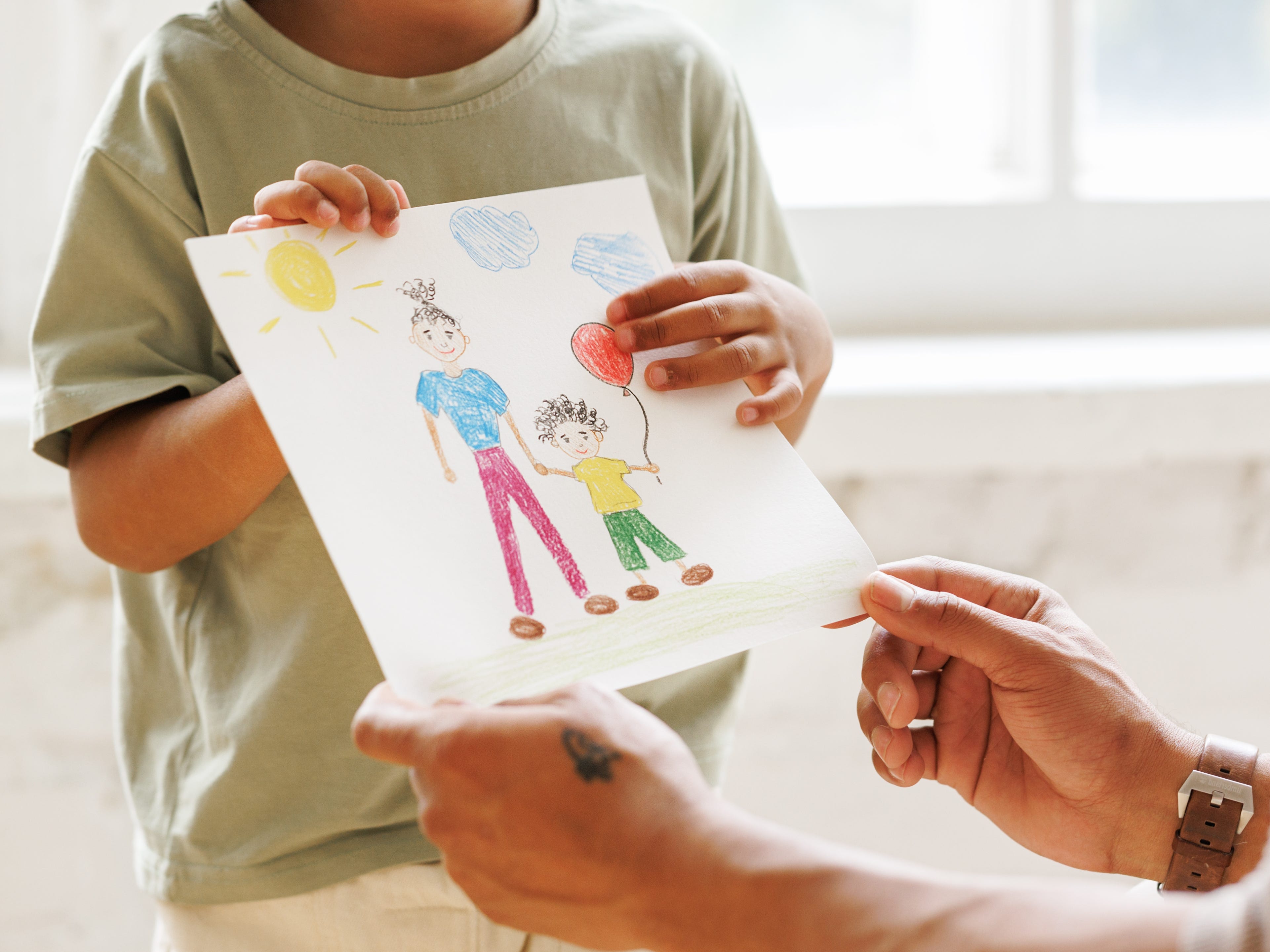 A close-up of a child handing an adult a drawing.