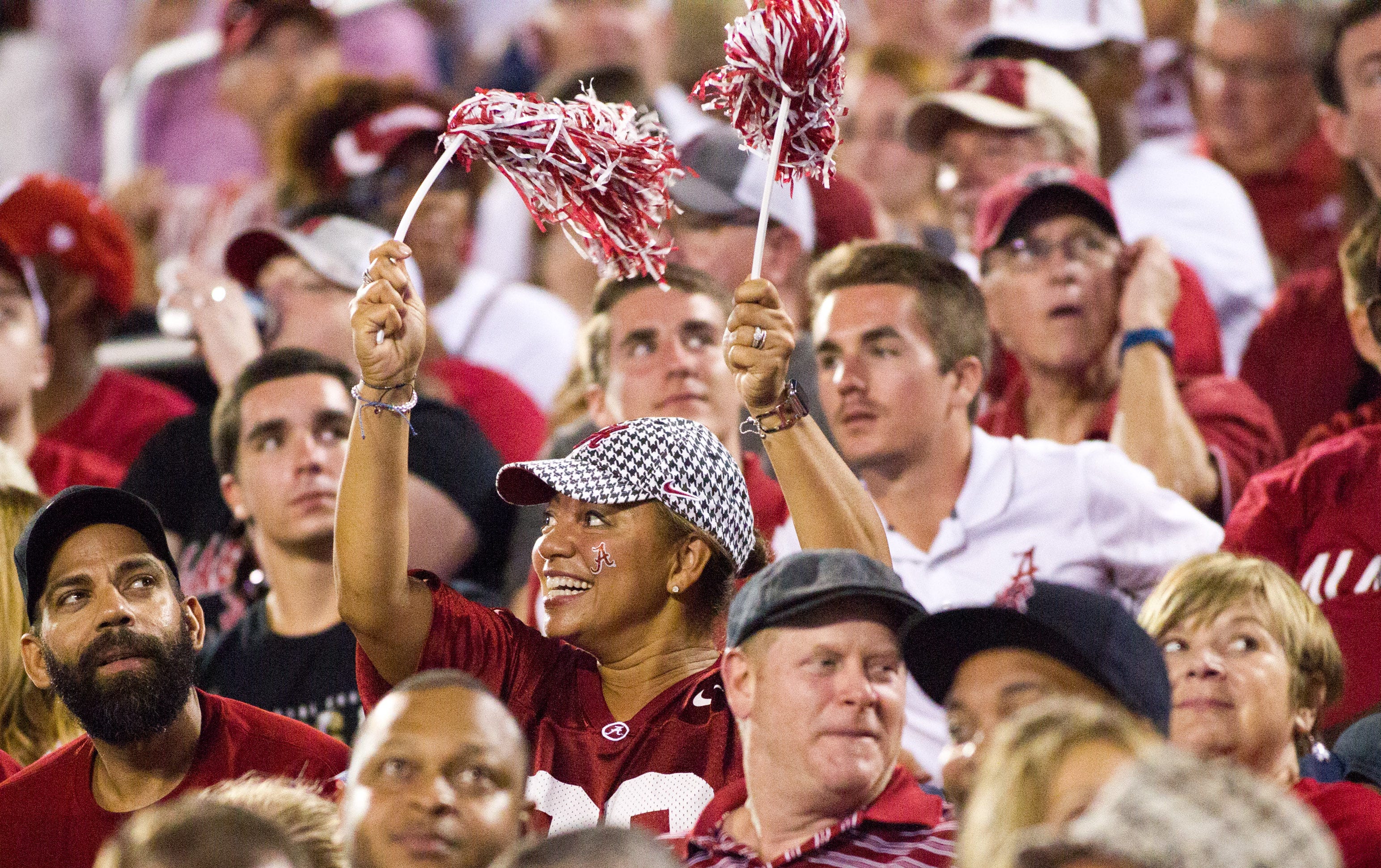 A crowd of people wearing red football shirts, with one woman waving red and white pom-poms.
