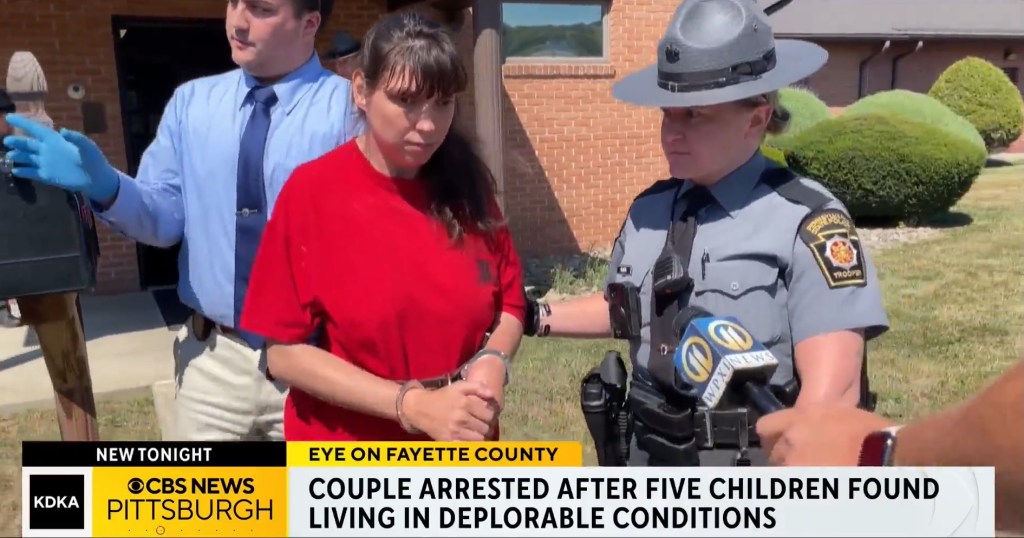 Woman in handcuffs being escorted by police after five children were found living in deplorable conditions.