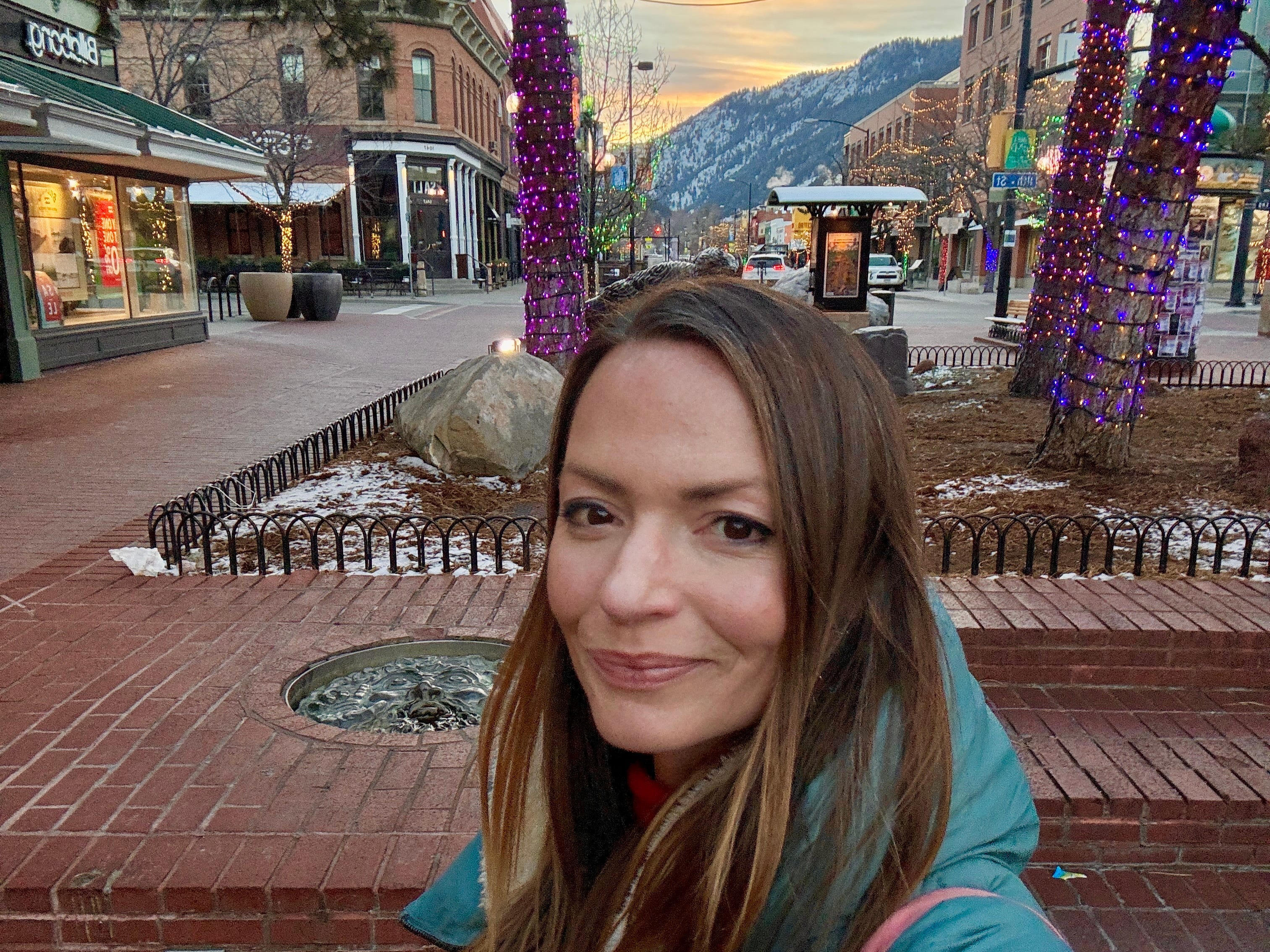 Emily taking a selfie in the center of town in Boulder, Colorado, with mountains in the distance.