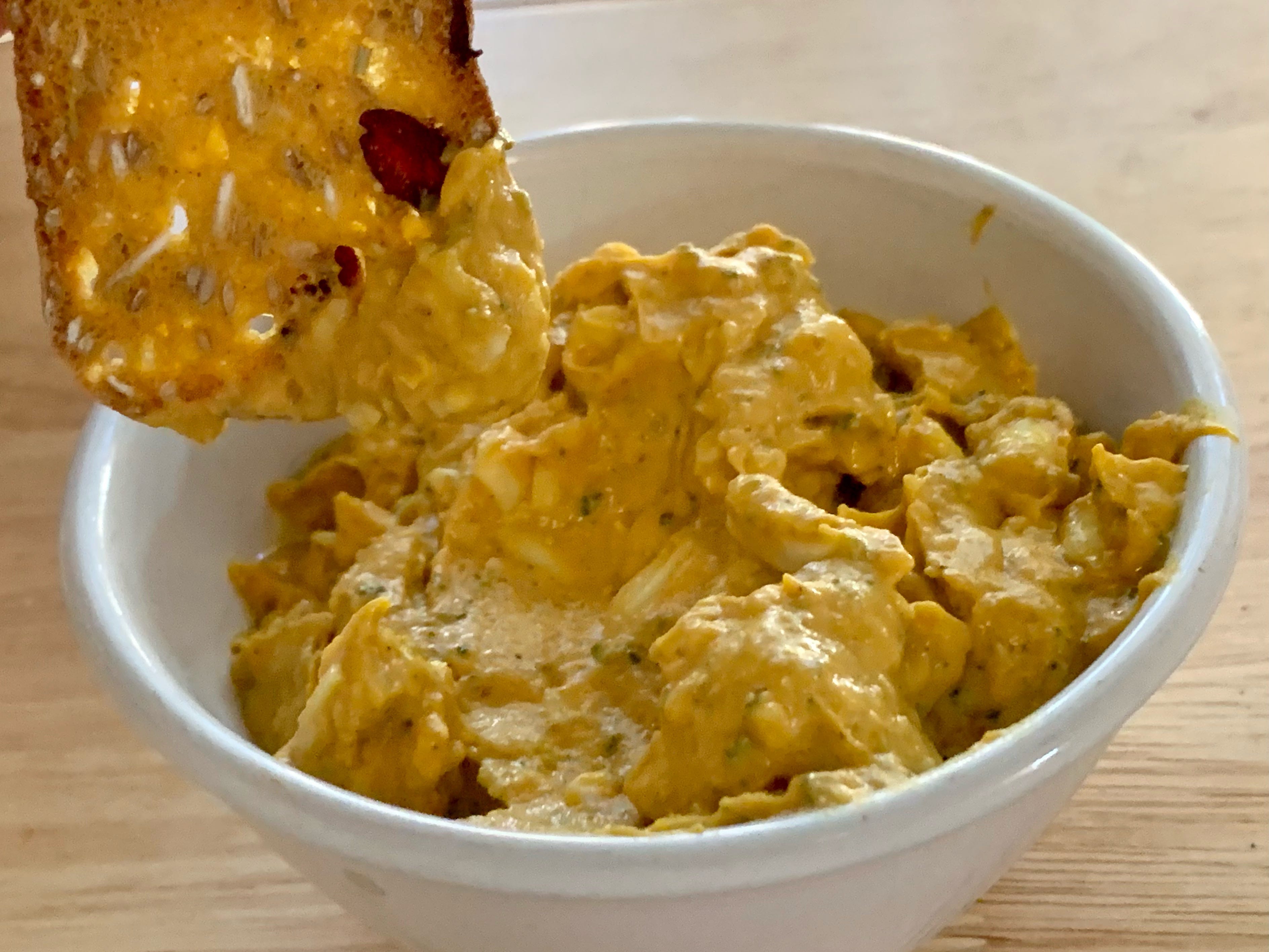 A chip being dipped into a small white bowl of Trader Joe's pumpkin greek yogurt cheese dip
