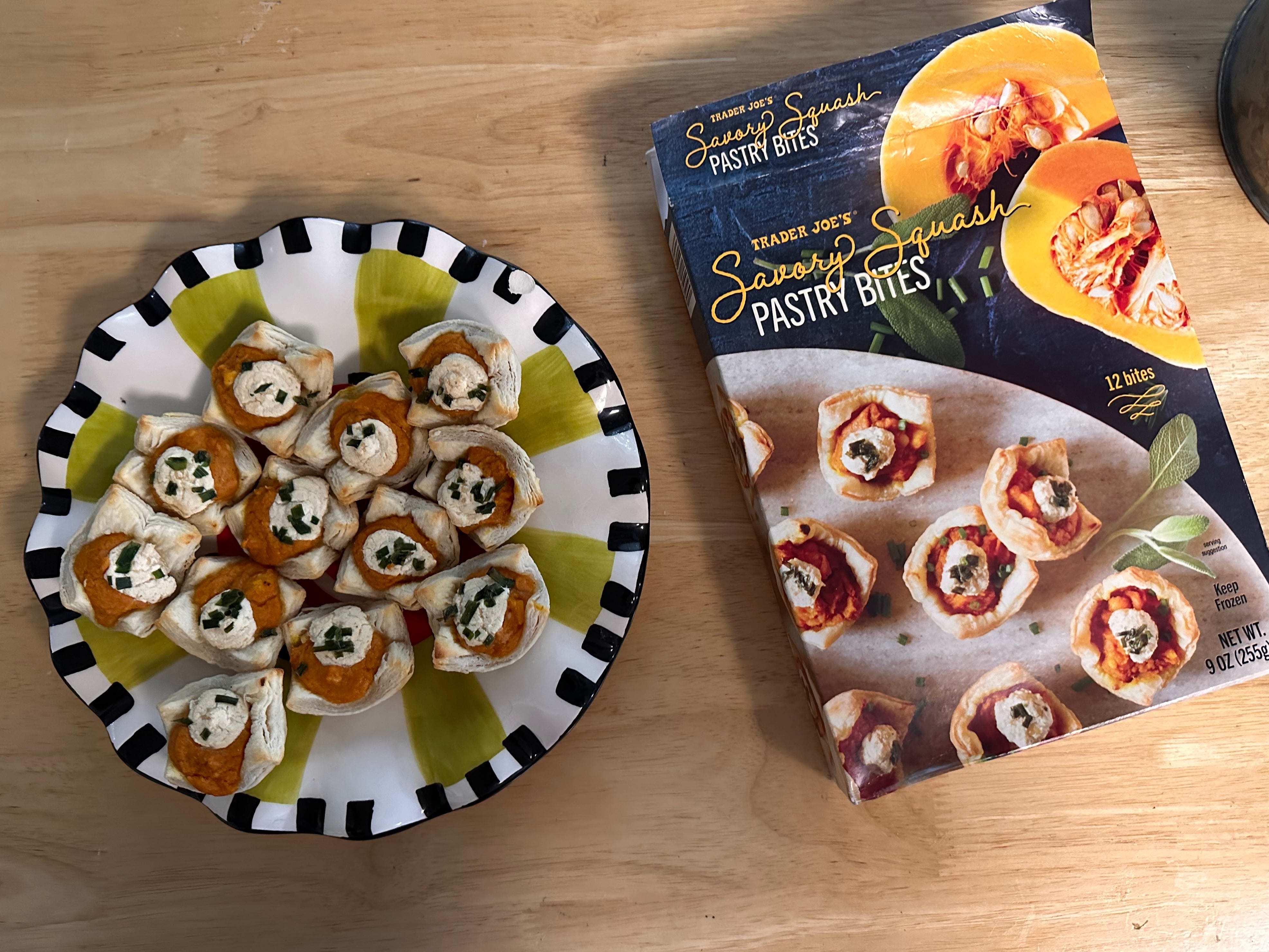 Trader Joe's savory squash pastry bites box next to plate filled with tiny tarts with pumpkin, marscapone, and chive on top