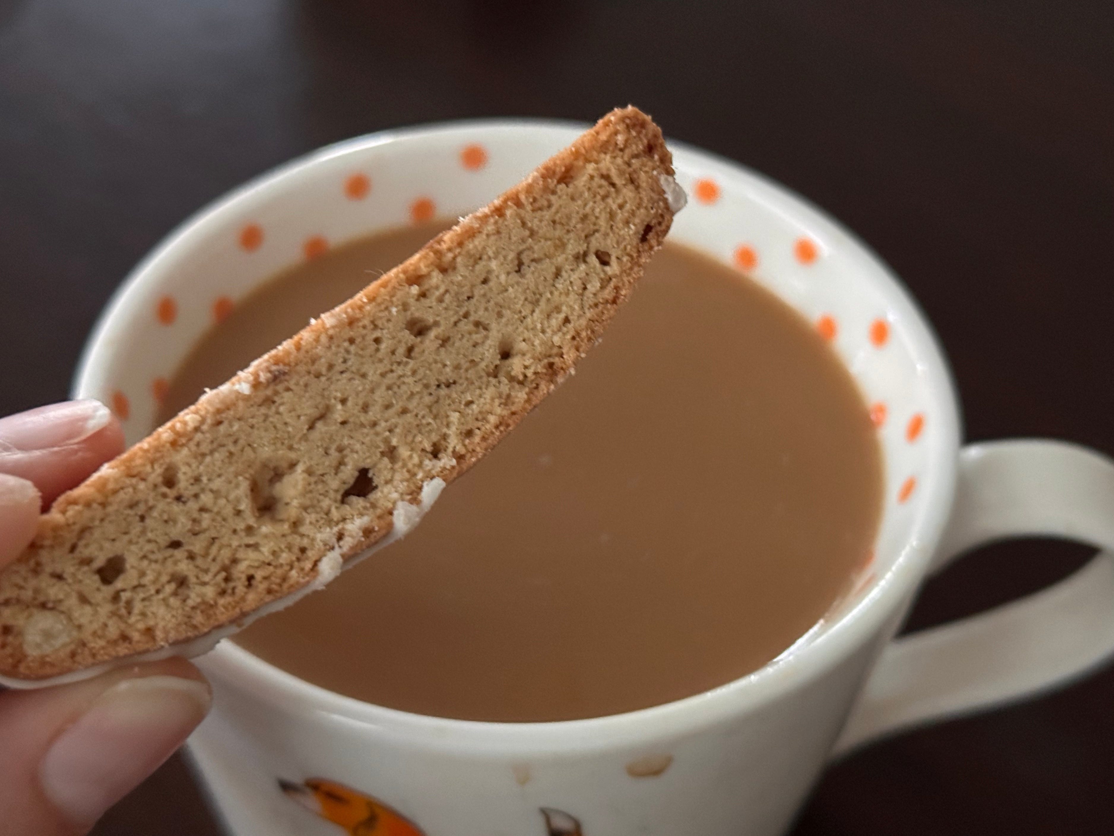 A piece of biscotti being held above a cup of coffee