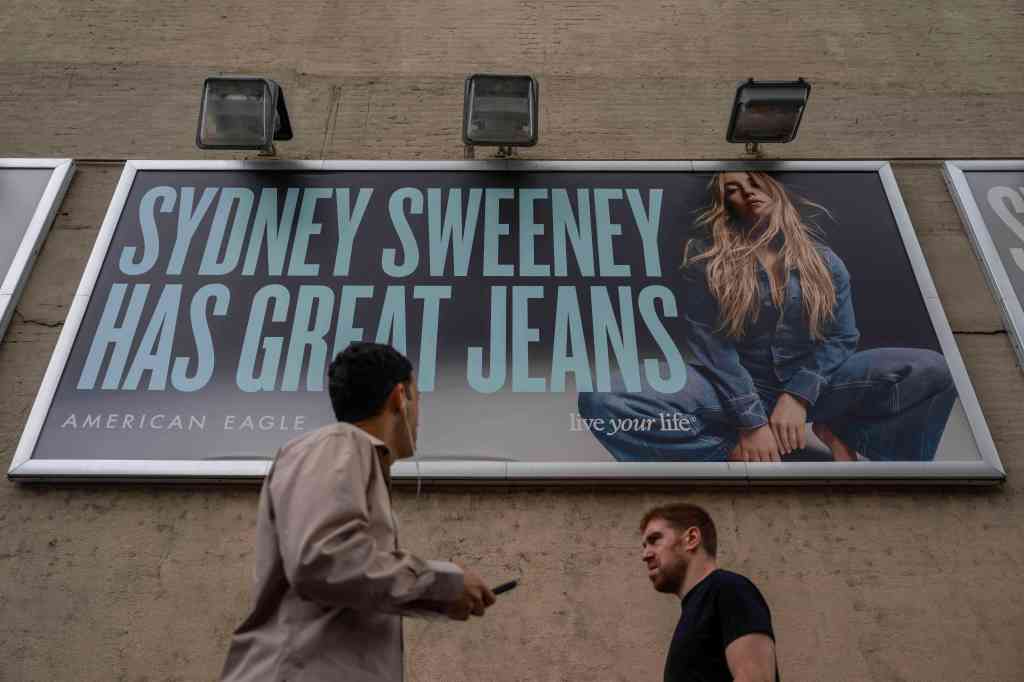 People walk past a campaign poster starring Sydney Sweeney which is displayed at the American Eagle Outfitters store