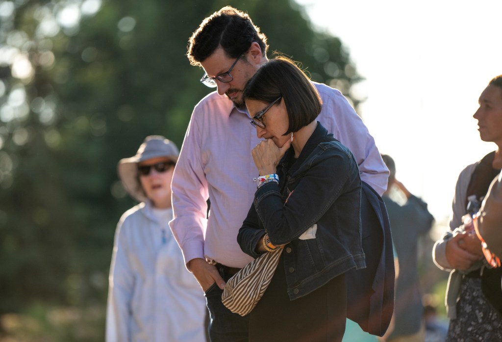 A man and woman stand close together, appearing somber.