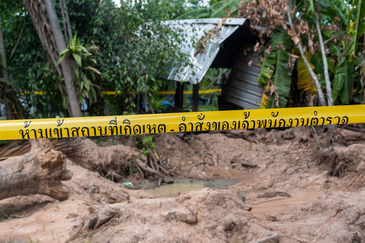 Yellow tape marks off a muddy crater with a fallen tree and damaged metal roof.