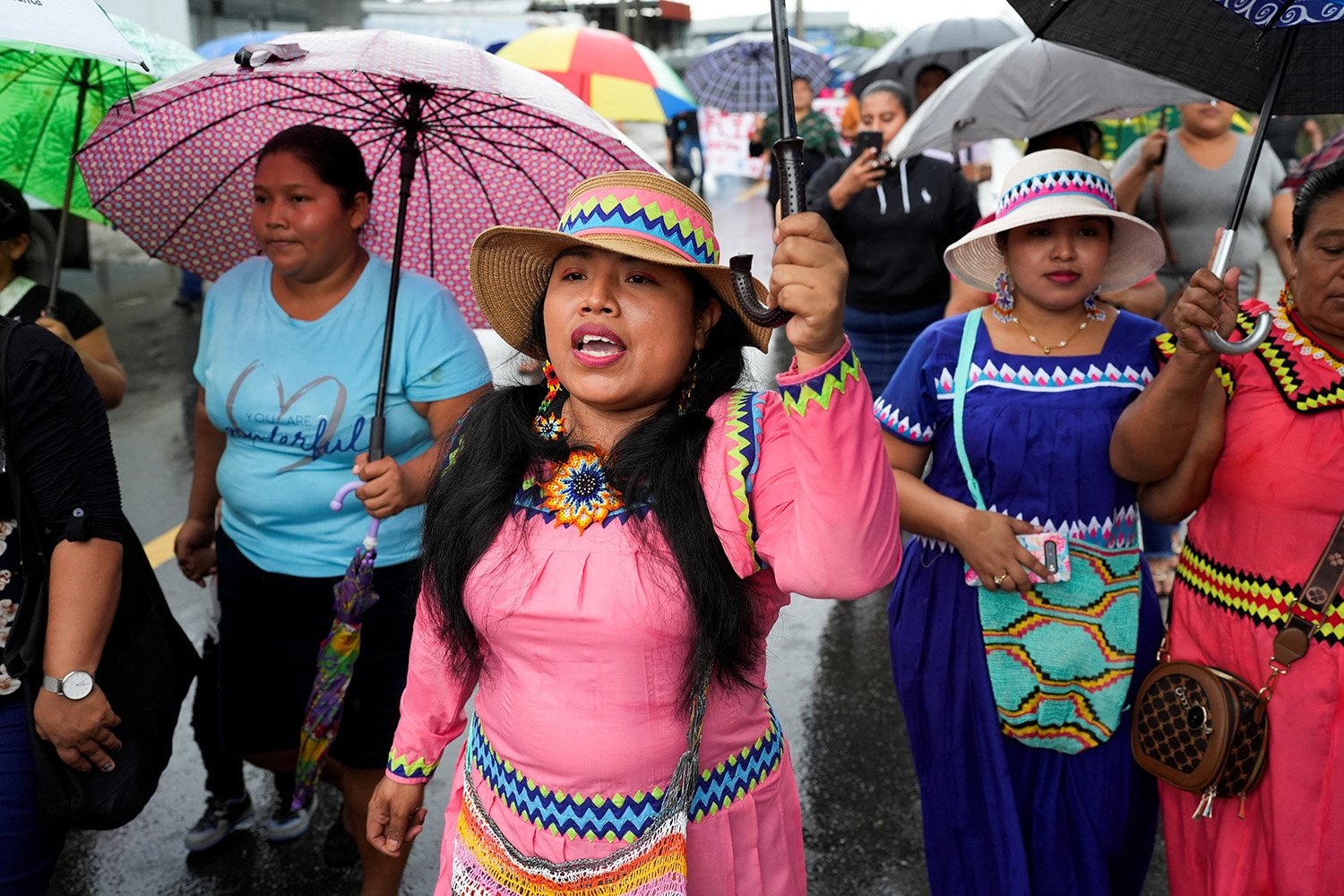 Women in colorful dresses hold umbrellas.
