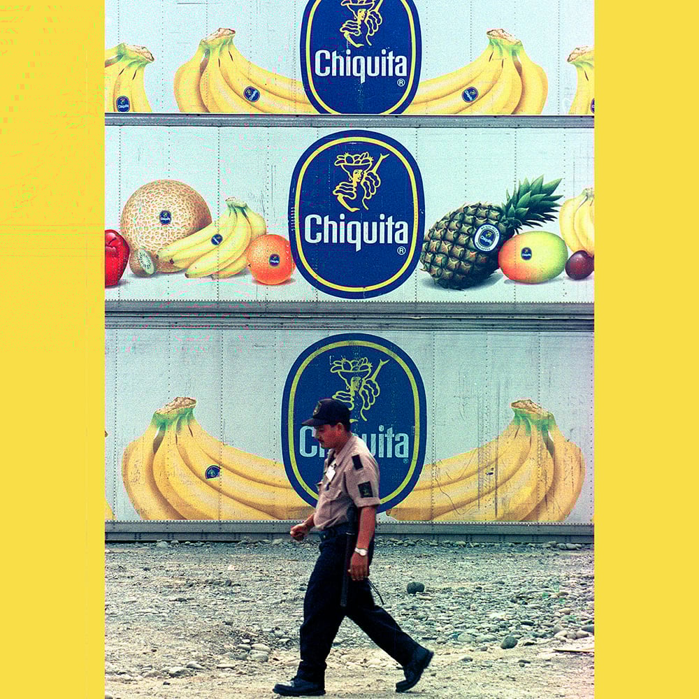 A person walks pass three tiers of containers with images of bananas, pineapples and other fruits and the Chiquita logo on them.