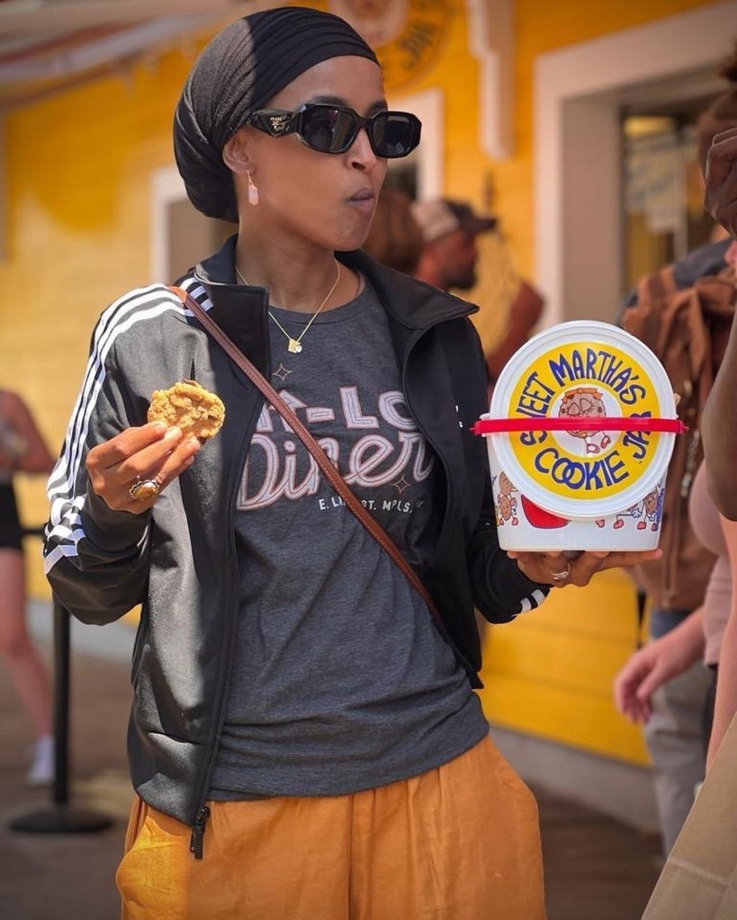 Ilhan Omar at the Minnesota State Fair, eating a cookie and holding a container of cookies.