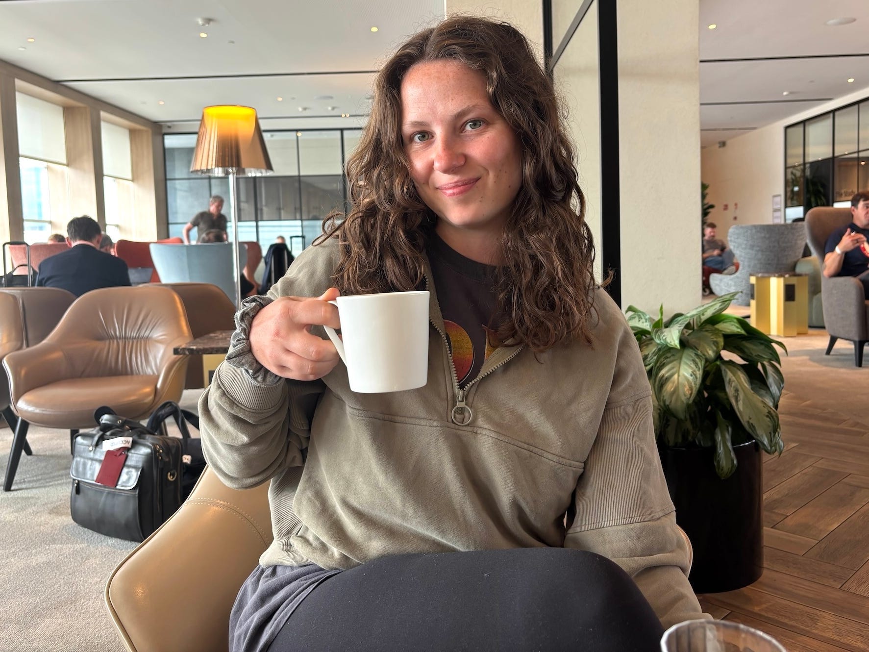 A woman holds a coffee cup and smiles in an airport lounge.