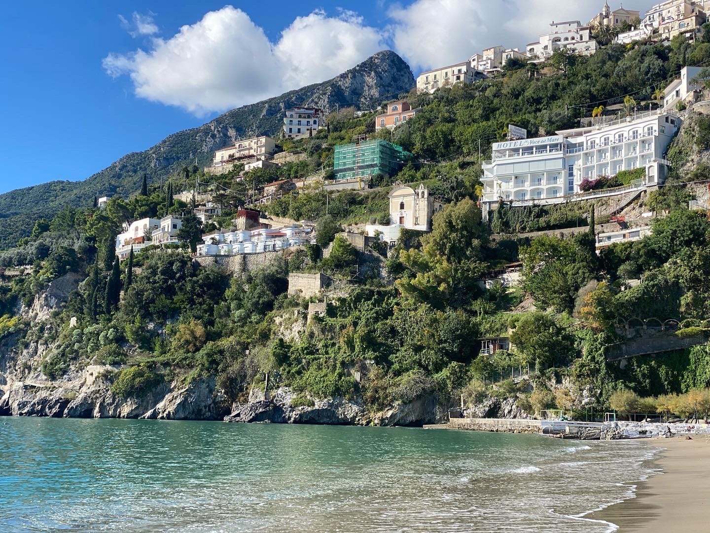 Buildings nestled along trees in cliffside above crystal clear water
