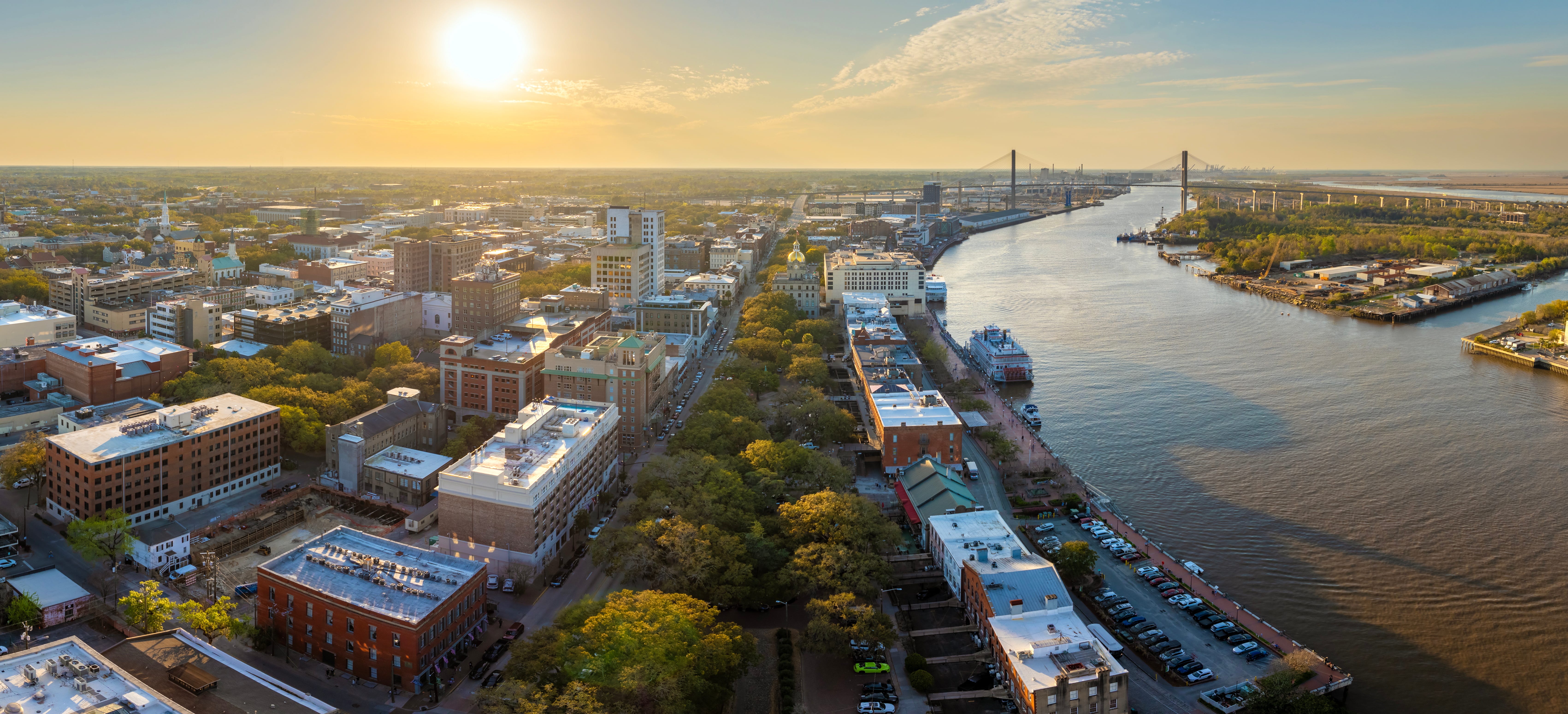 A sunset over the city of Savannah, Georgia, with a river and a bridge.