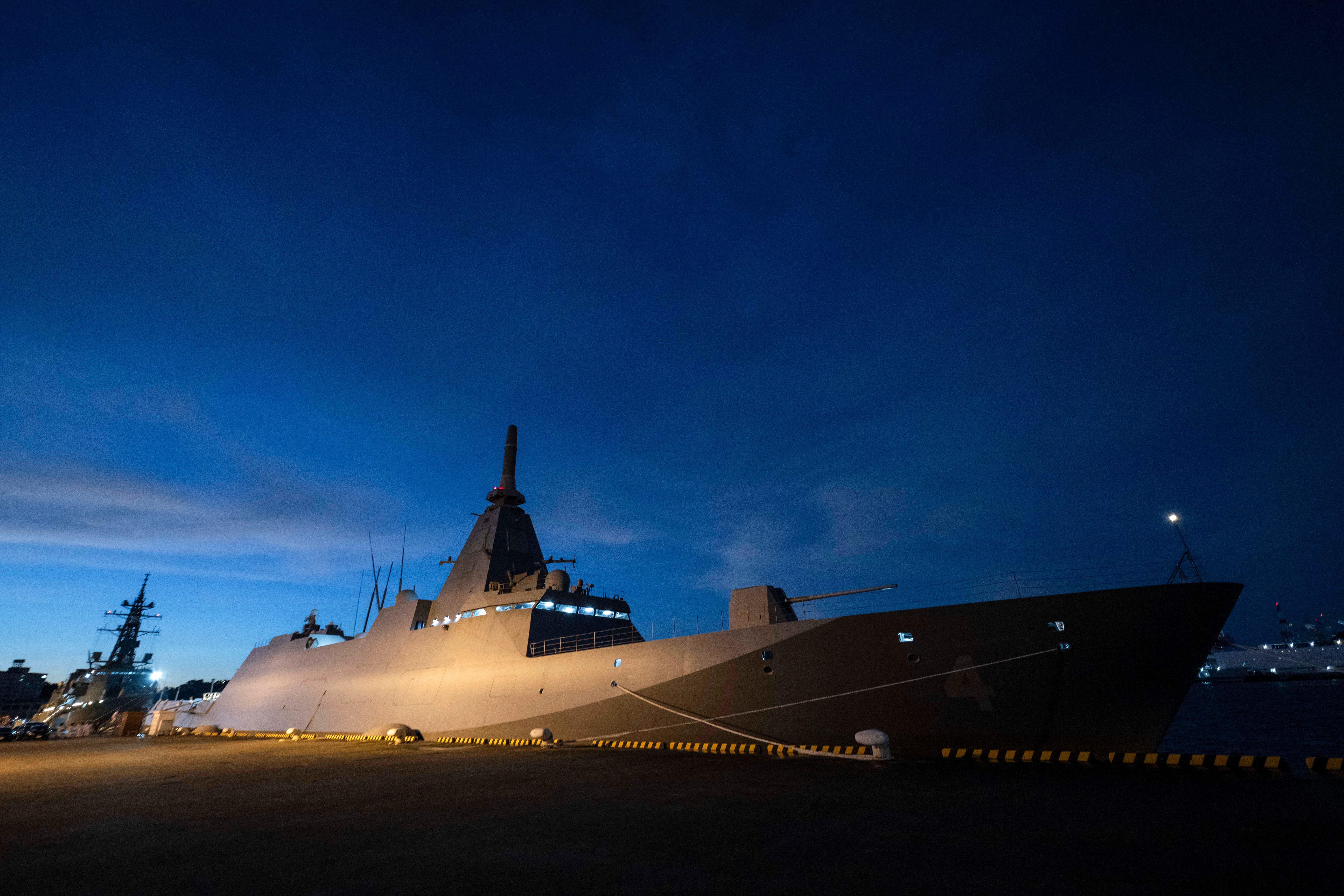 A side view of a grey Japanese warship seen docked at night with a dark blue sky in the background.