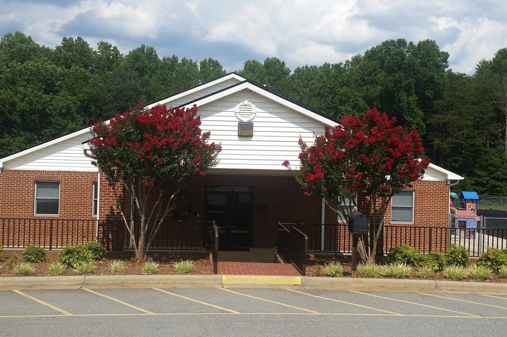 Brick building with red flowering trees and a playground in the background.