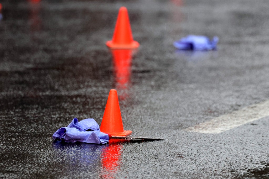 Crime scene with orange cones, a knife, and discarded gloves in the rain.