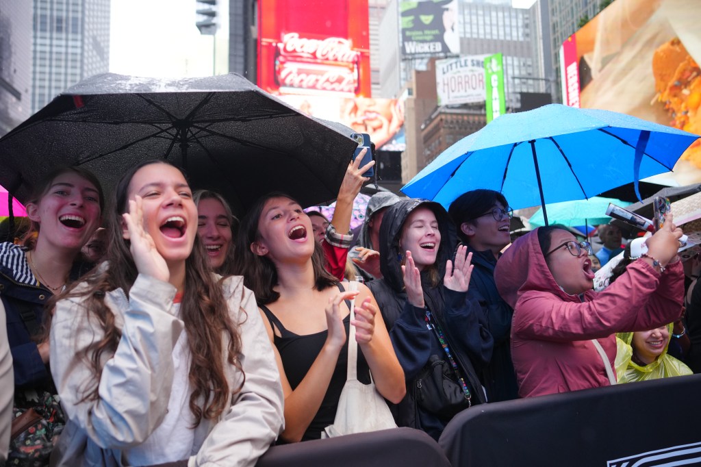 Excited concertgoers in Times Square under umbrellas.