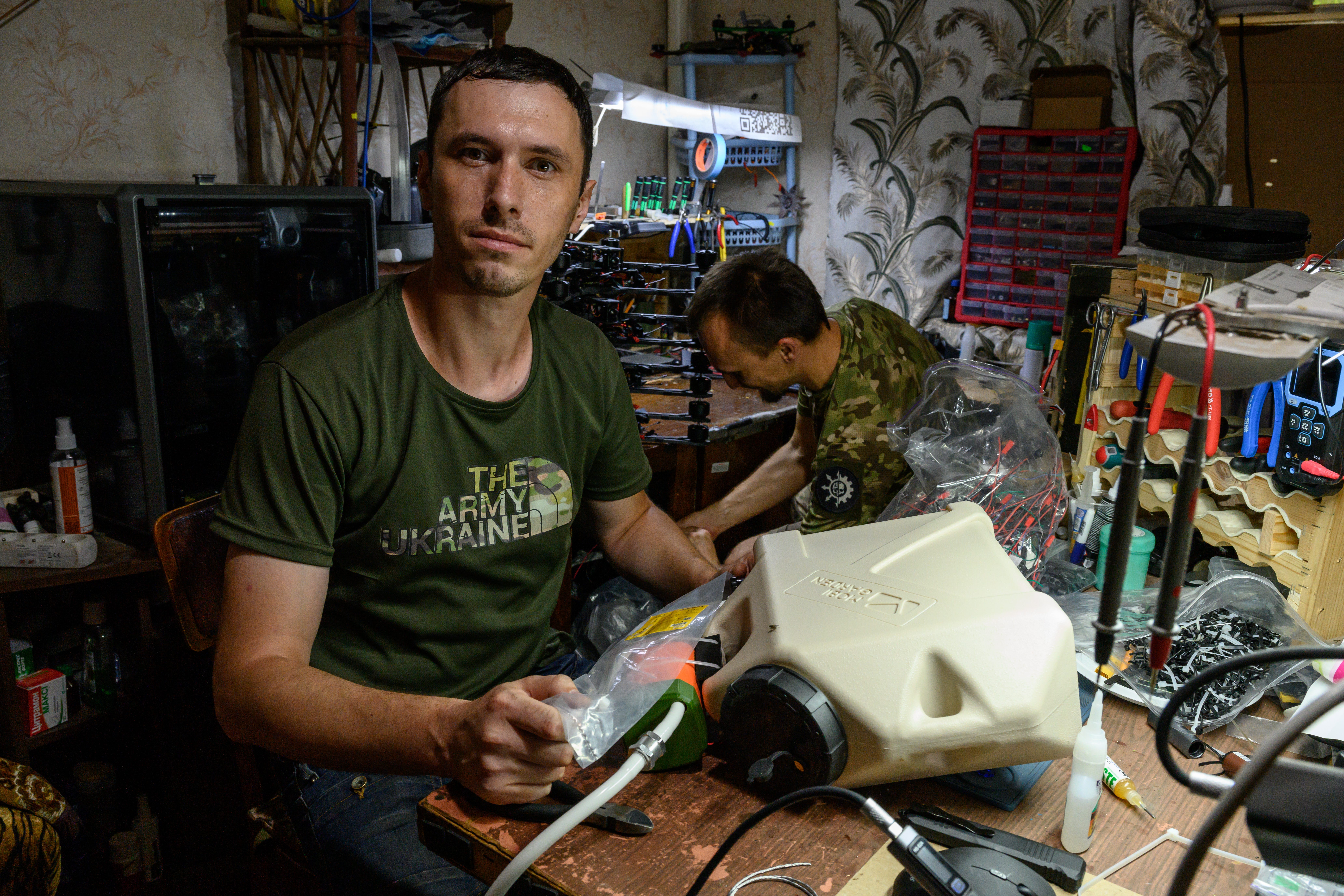 Two Ukrainian soldiers work on FPV drones together in a workshop.