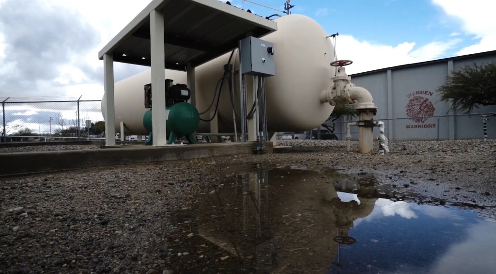 Large tanks and a compressor under a shelter; puddle reflects the scene.