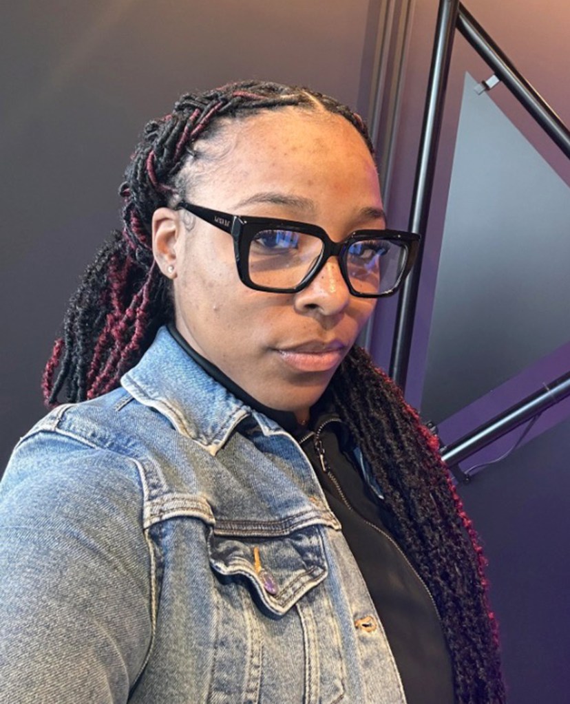Portrait of a woman wearing black-framed glasses and a denim jacket.