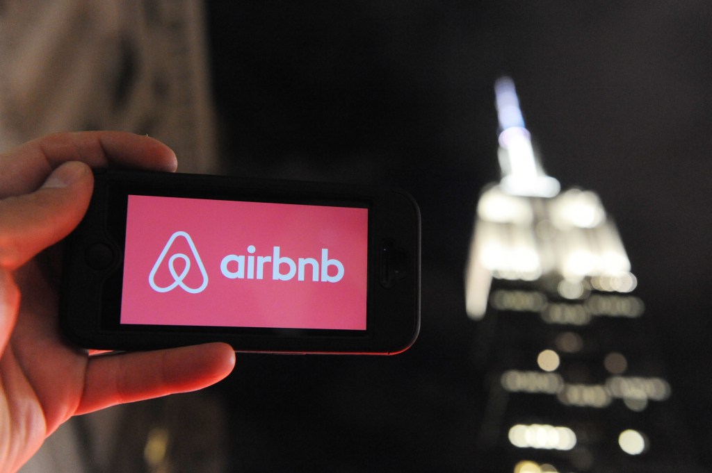 The Airbnb logo glows on a phone with the Empire State Building in the background, as the company battles critics who say it drains housing supply.