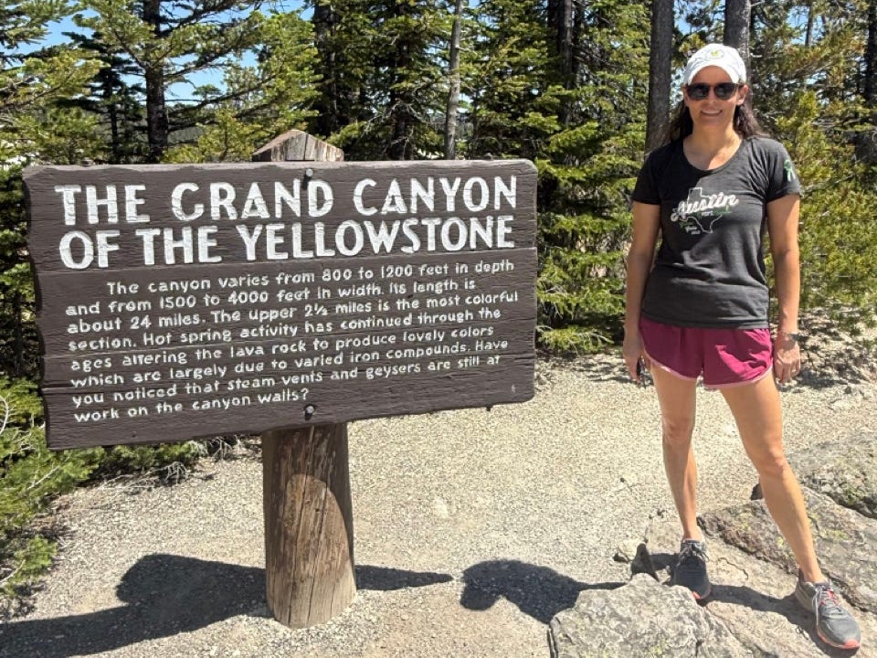 Woman standing next to "The GRand CAnyon of the Yellowstone" sign