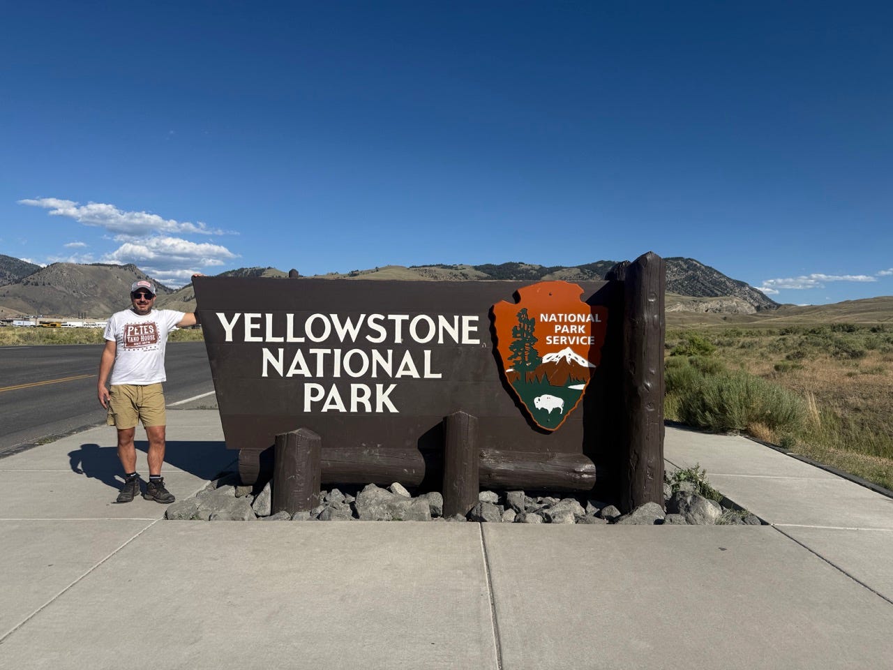 Author Ash Jurberg leaning on Yellowstone entrance sign