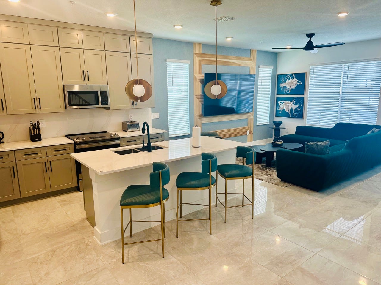 Large kitchen with shiny tile, three barstools, white marble island next to living room area