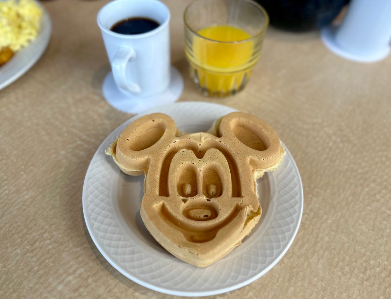 Mickey mouse head waffle on plate next to orange juice, coffee