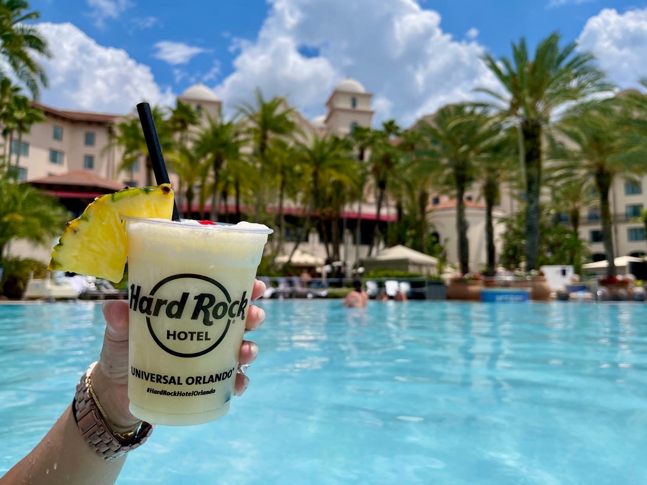 Hand holding frozen cocktail with pineapple wedge at Hard Rock Hotel written on cup in front of pool