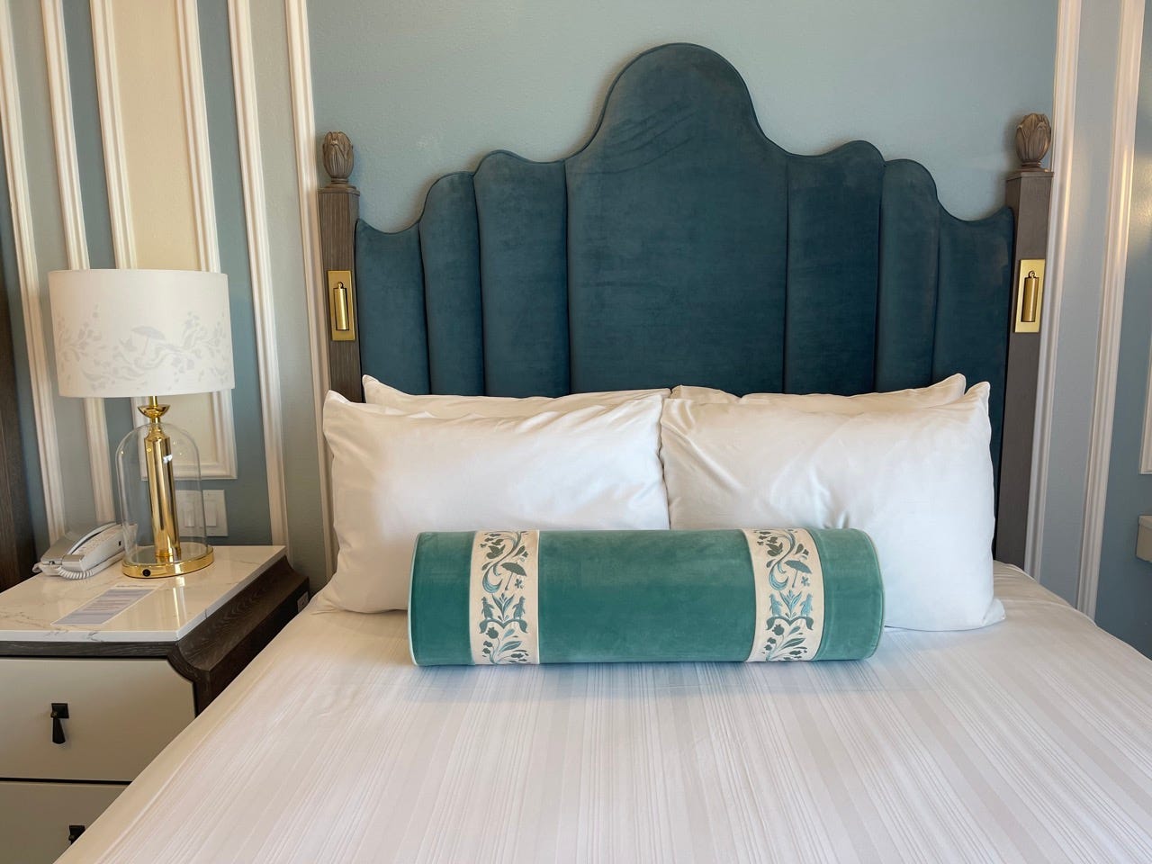 Bed in room at Grand Floridian hotel with blue tufted headboard, white pillows, cylinder pillow