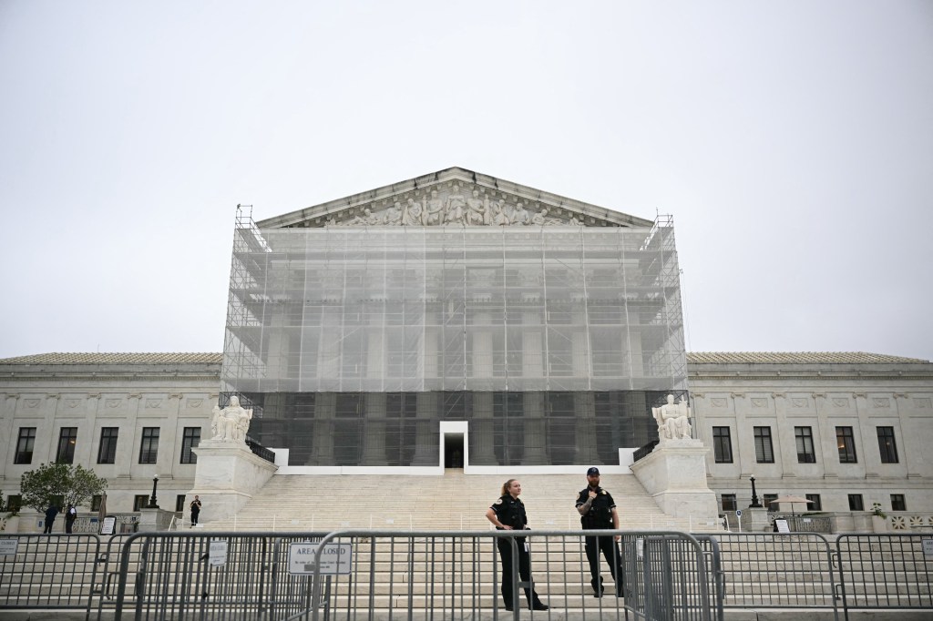 The US Supreme Court building covered in scaffolding with police officers standing guard.