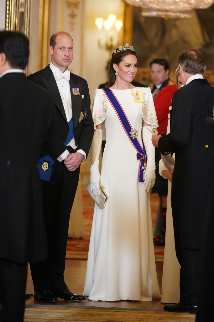 Prince William in tails and a blue sash and medals, Kate Middleton in a white gown and blue sash and medals and tiara and white gloves.