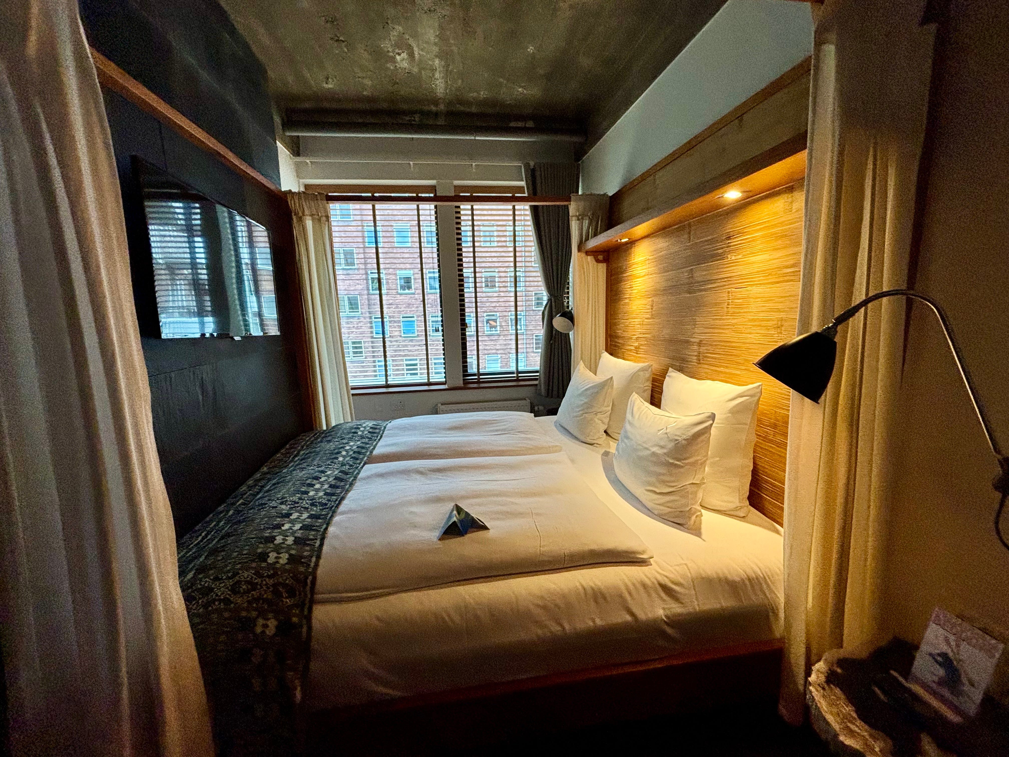 A bed with curtains around it. A TV is mounted to the wall in front of the bed.