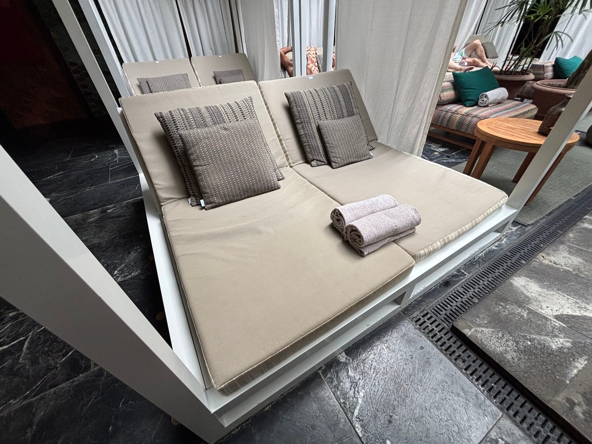 A cabana with cushions for two people. Two towels sit on the cabana.