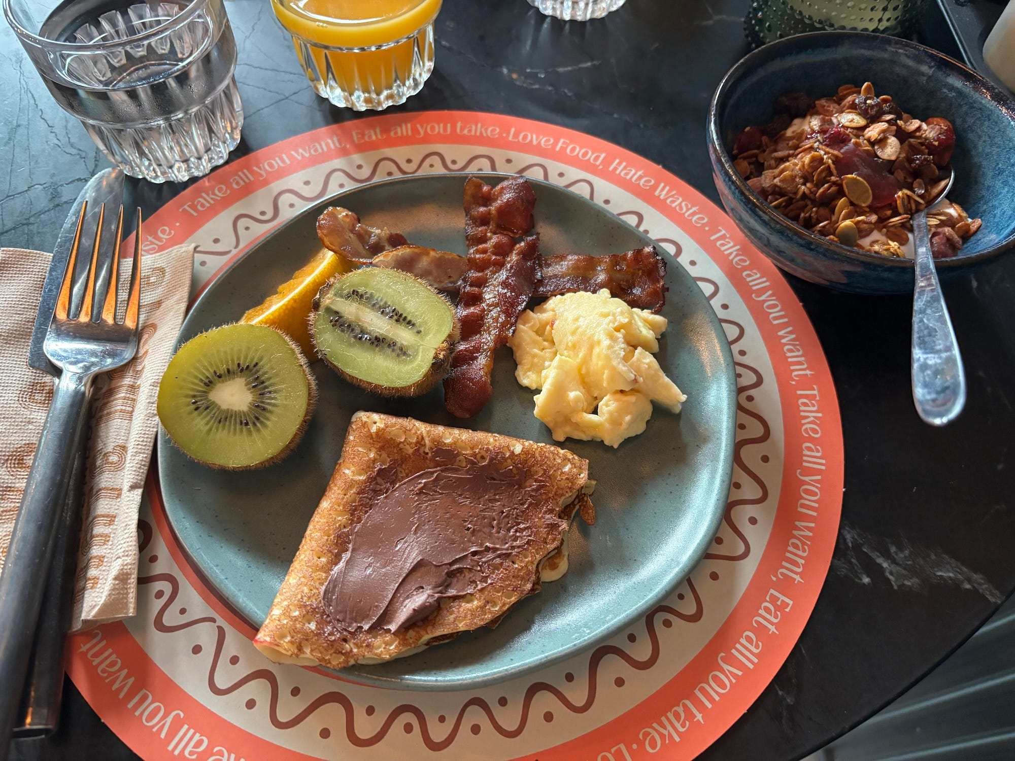 A breakfast spread with fruit, pancakes, bacon, eggs, and yogurt.