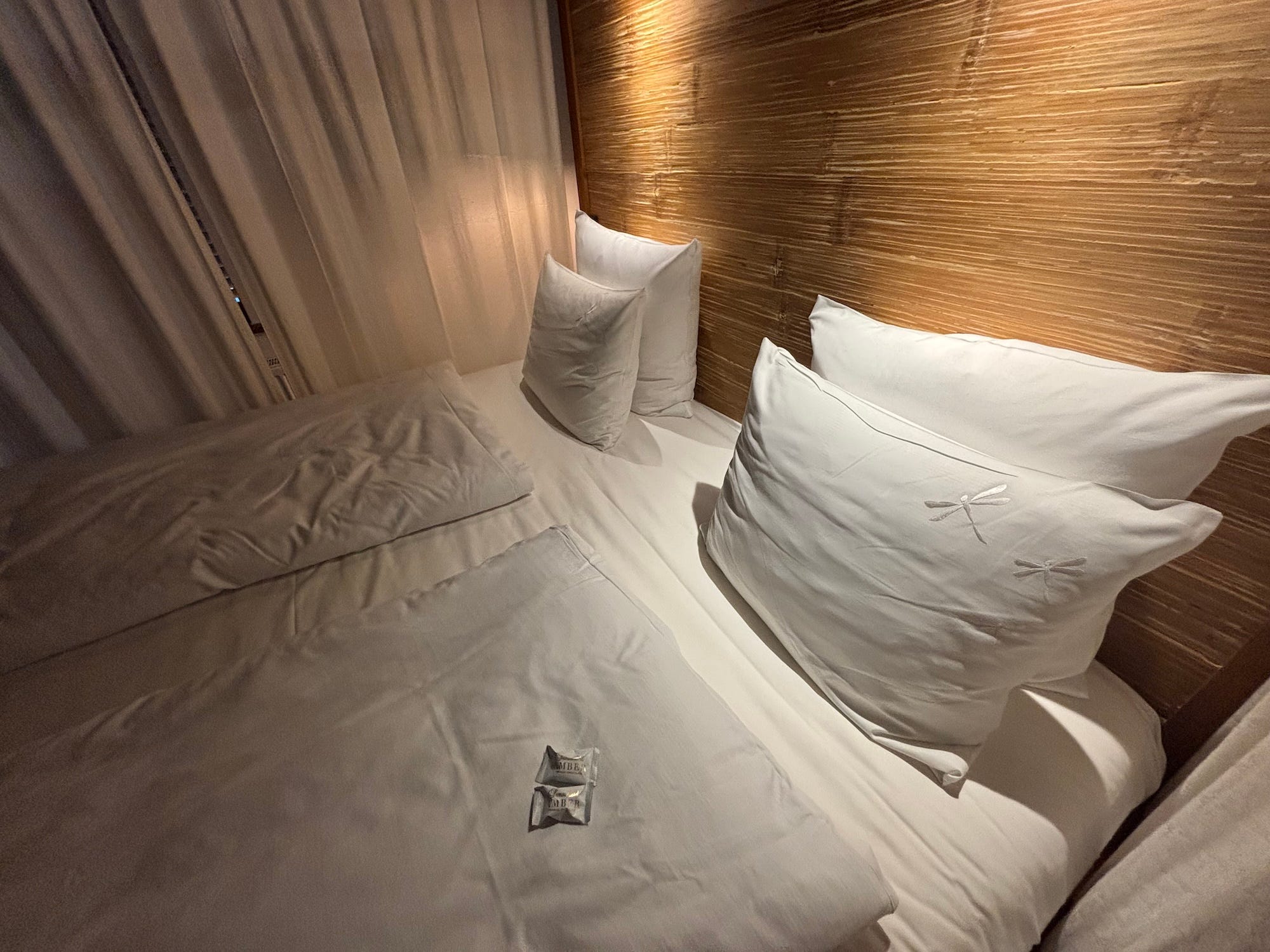 A bed with two duvets and four pillows. Two chocolates sit on the mattress.