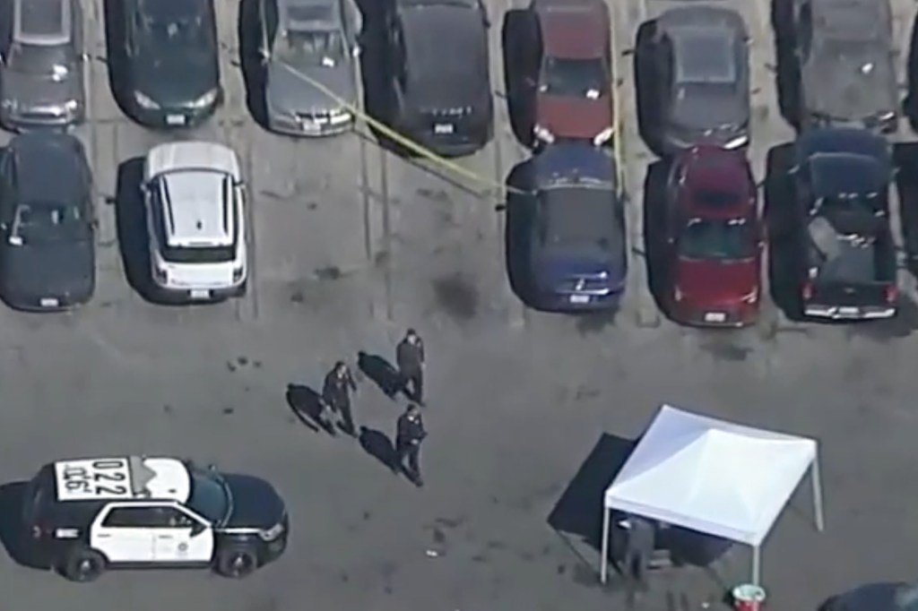 Aerial view of a crime scene in a parking lot with police officers and a forensic tent.