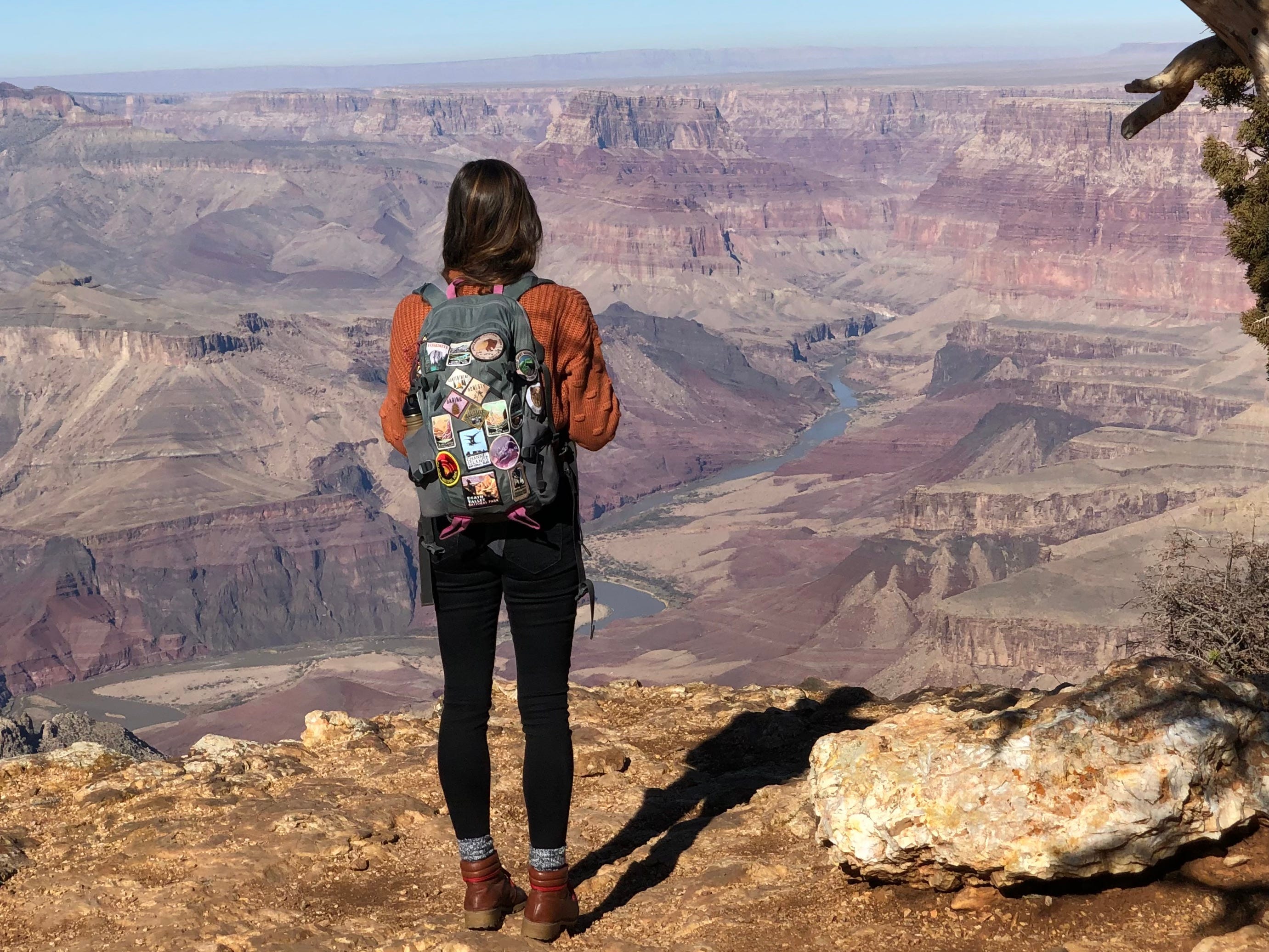 Emily, wearing a backpack covered in patches, looks out at the Grand Canyon.
