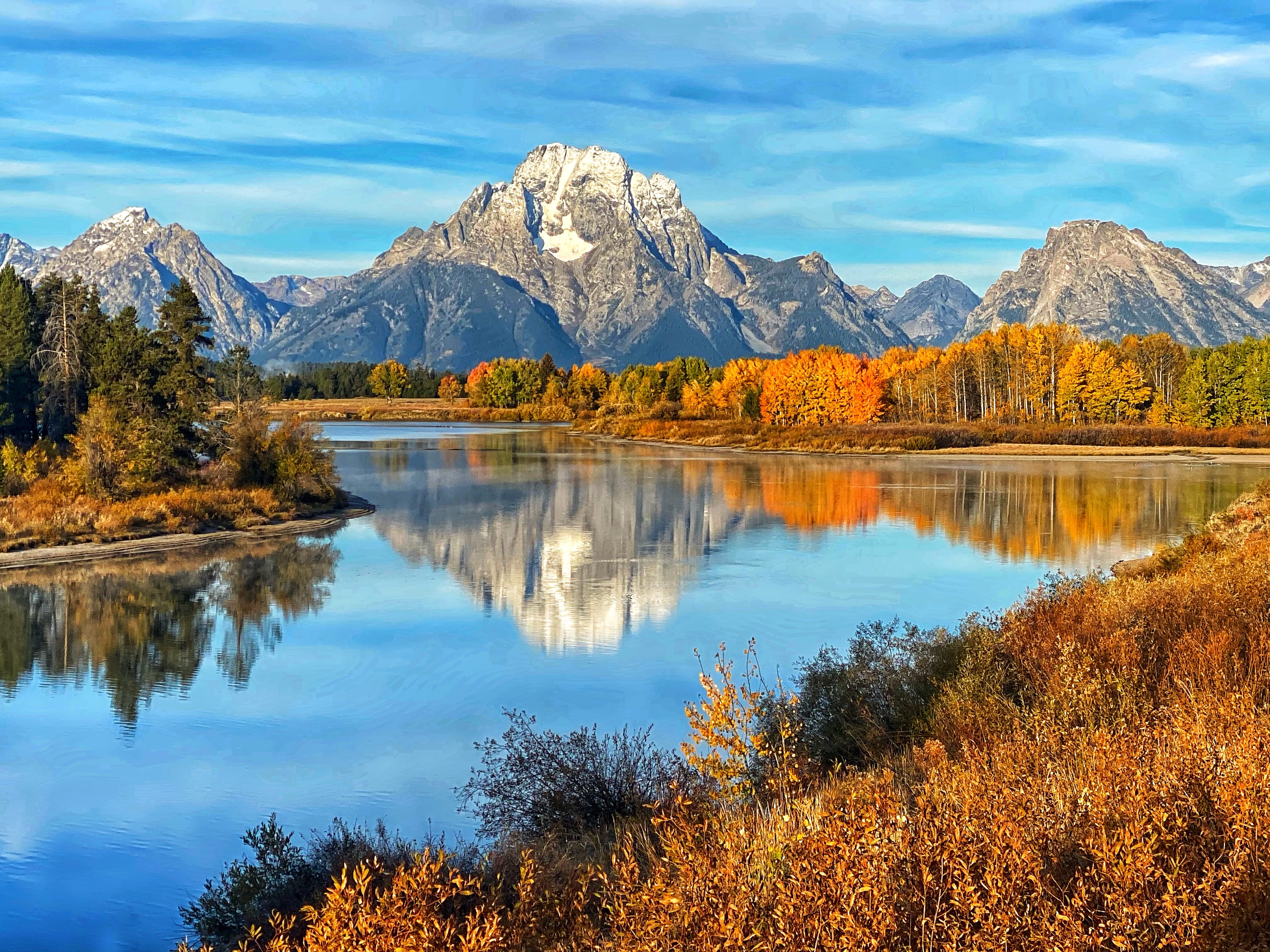 Mountains and trees with autumn leaves surround a lake in Grand Teton National Park.
