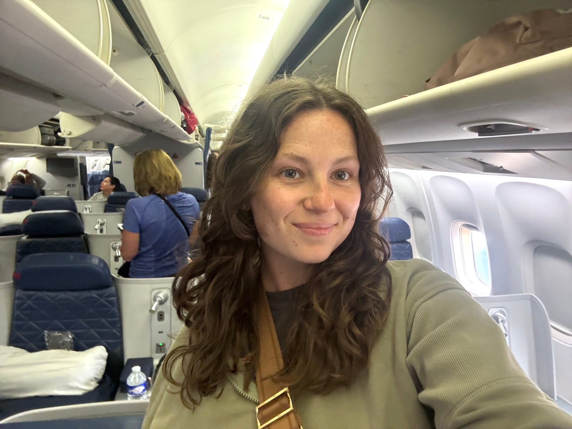 A selfie of a woman standing in the business class section of a Delta One cabin of a plane.