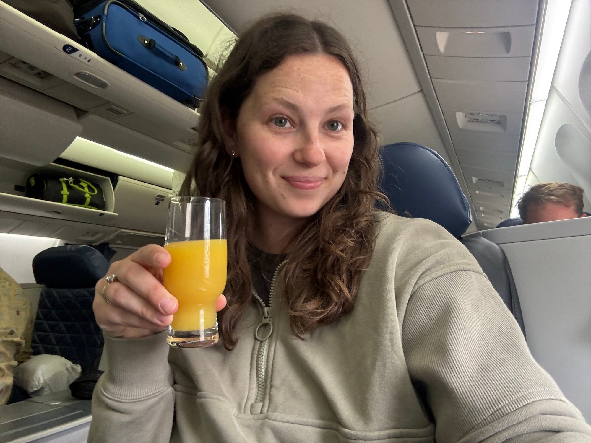 A woman takes a selfie on a plane holding a mimosa.
