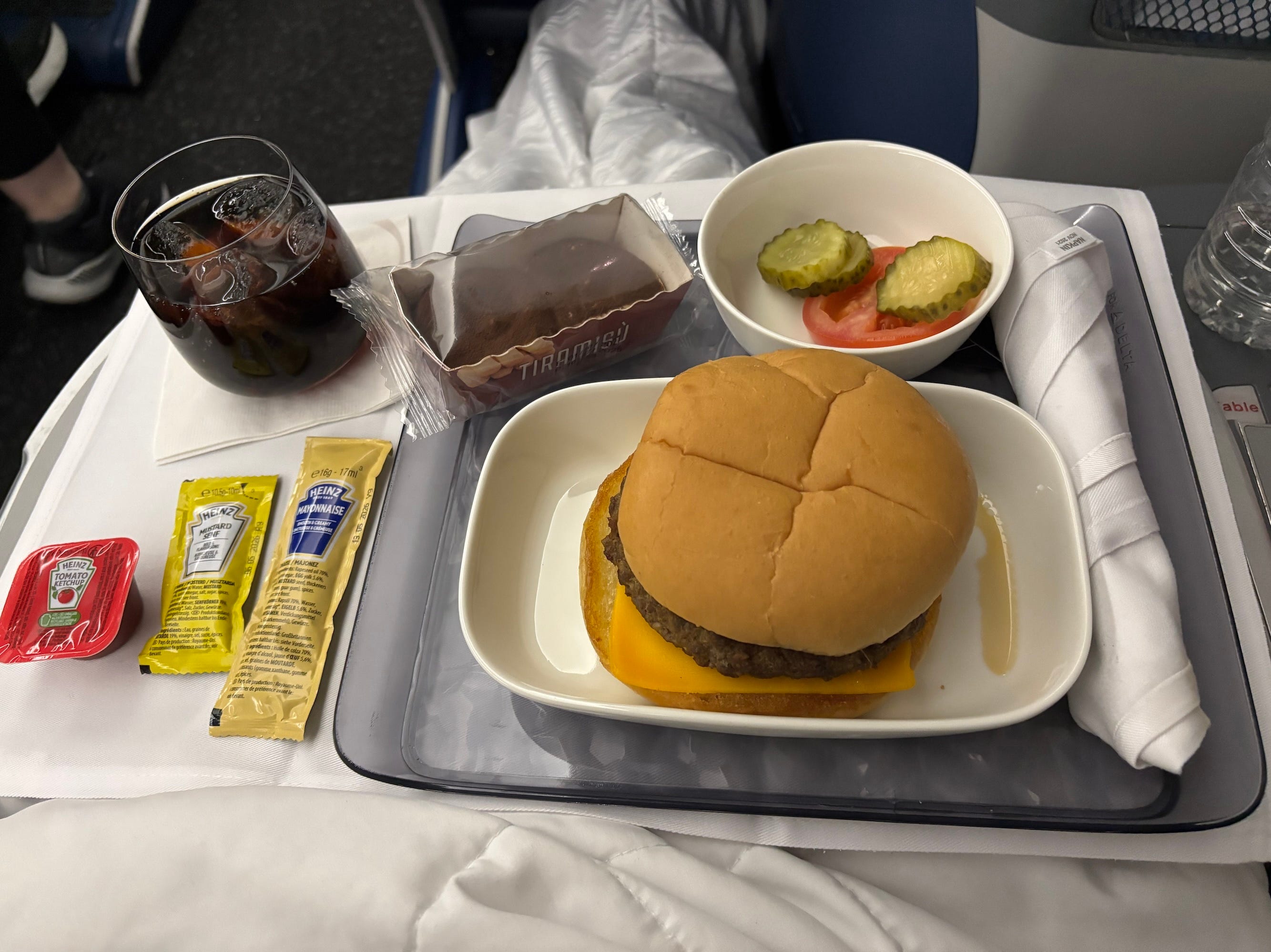 A tray of food on an airplane containing a burger and a pre-packaged tiramasu.