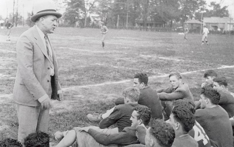 Knute Rockne, shown giving a pep talk to a group of football players, is buried at the cemetery.