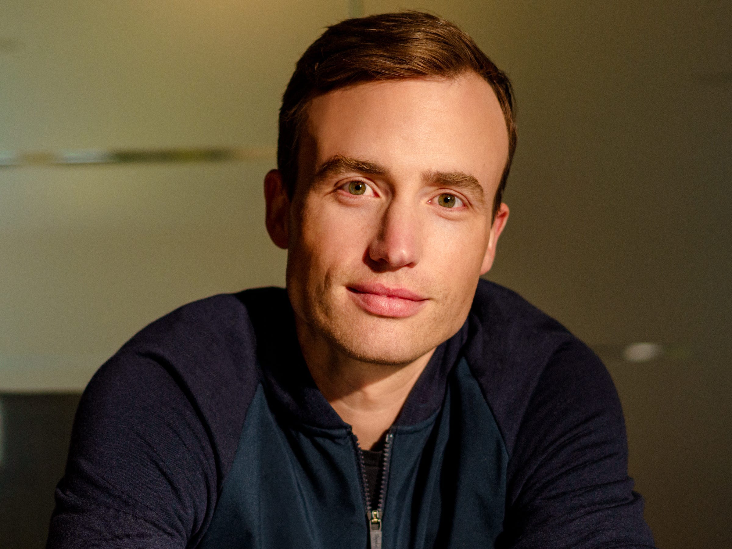 Andrew Reed sitting at a table with his arms crossed, wearing a blue zip-up sweater.