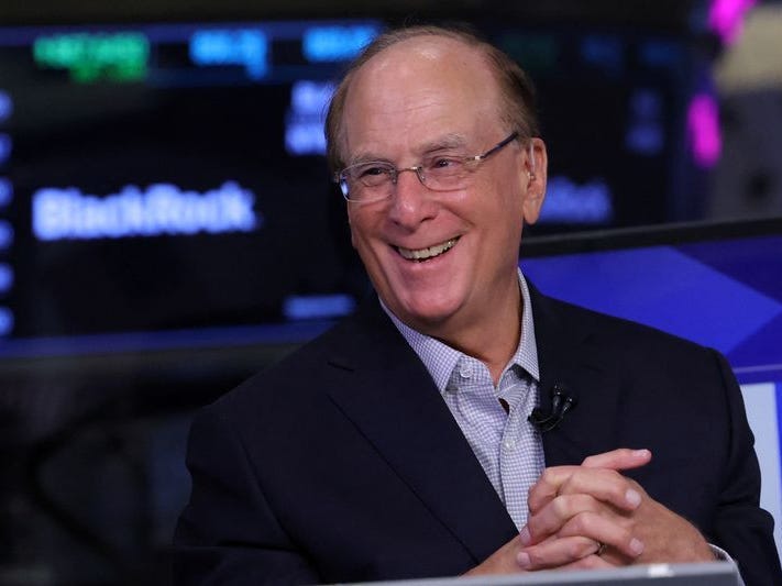 BlackRock CEO Larry Fink smiles in front of a blurry BlackRock logo.