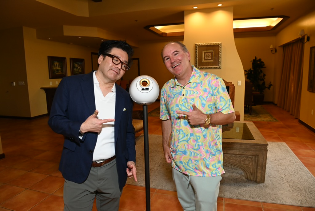 Two men stand on either side of a Worldcoin orb, pointing at it.